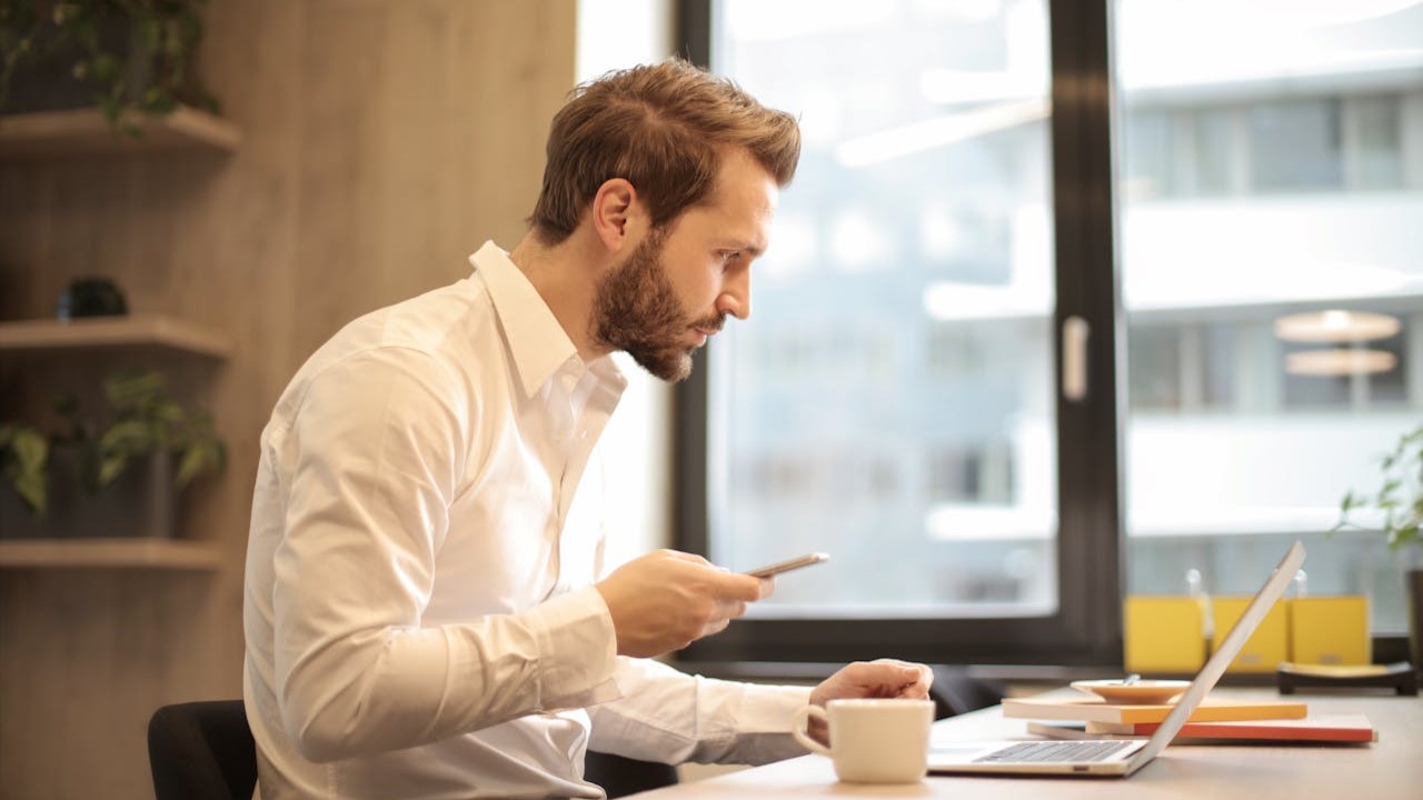 Man in wit overhemd werkt gefocust op laptop aan bureau, mogelijk bezig met interimcontract taken