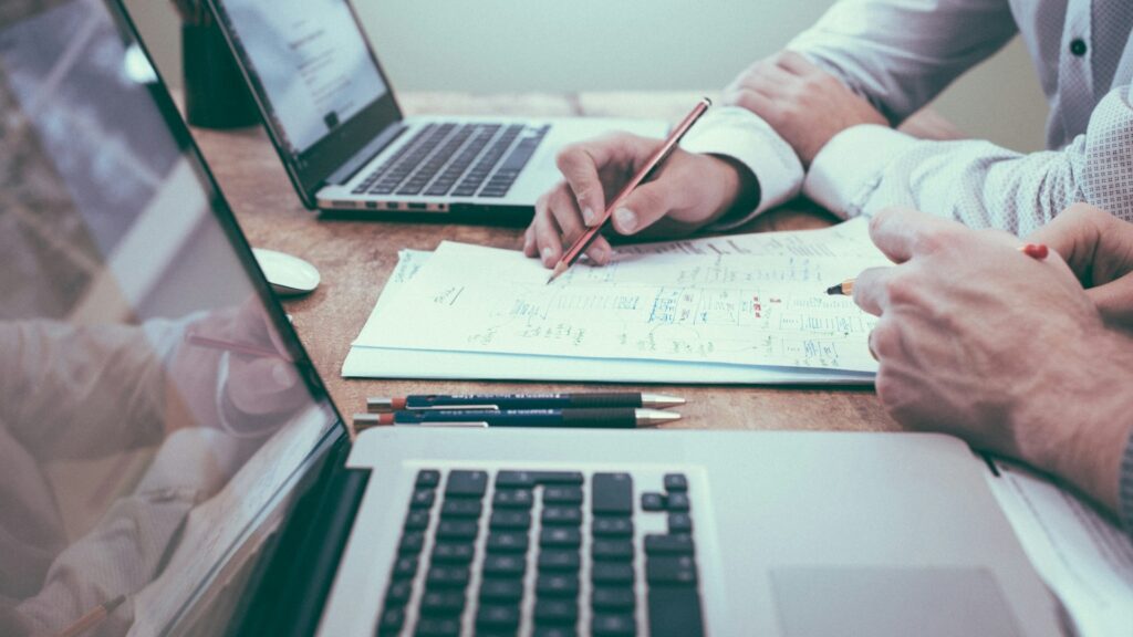 Twee personen analyseren technische documentatie en auditgegevens op laptops tijdens een security-audit