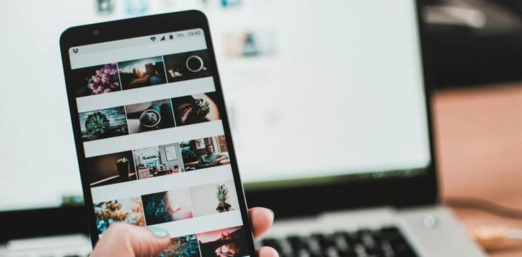 Persoon bekijkt Instagram-profiel op smartphone voor laptop, focus op foto's in rasterweergave