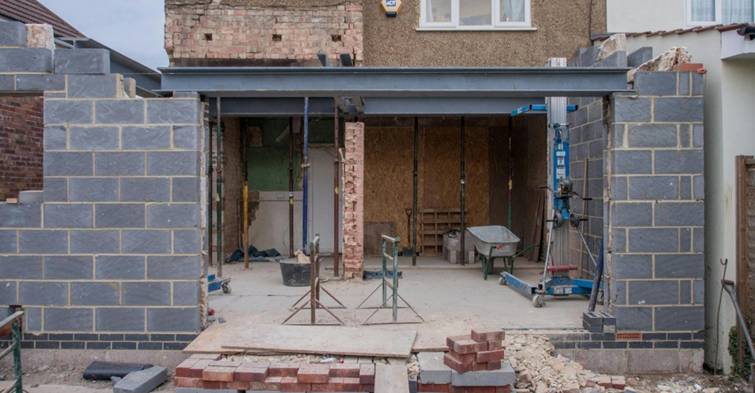 Uitbouw in aanbouw met stalen balken, betonvloer en deels gemetselde muren tijdens renovatie