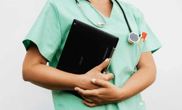 Zorgverlener in groen uniform houdt geruststellend de handen vast van een cliënt in de ouderenzorg
