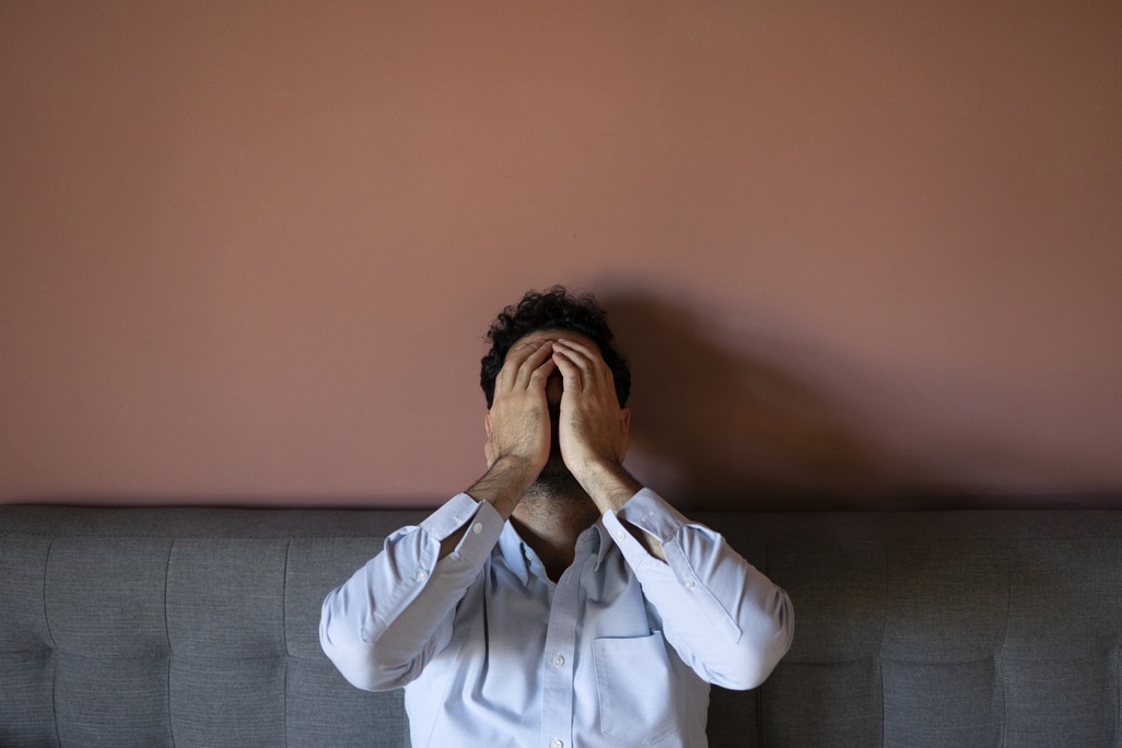 Man zit met zijn handen voor zijn gezicht op de bank door stress.